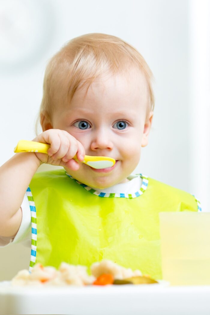 kid eating healthy food with a spoon at kitchen